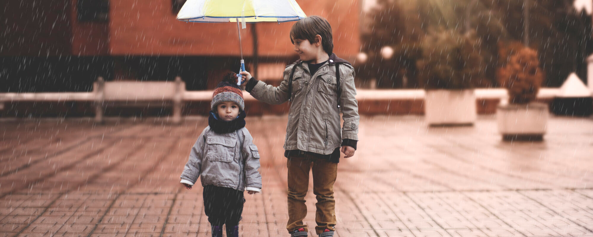 A little boy and his older brother protect themselves from the rain with an umbrella