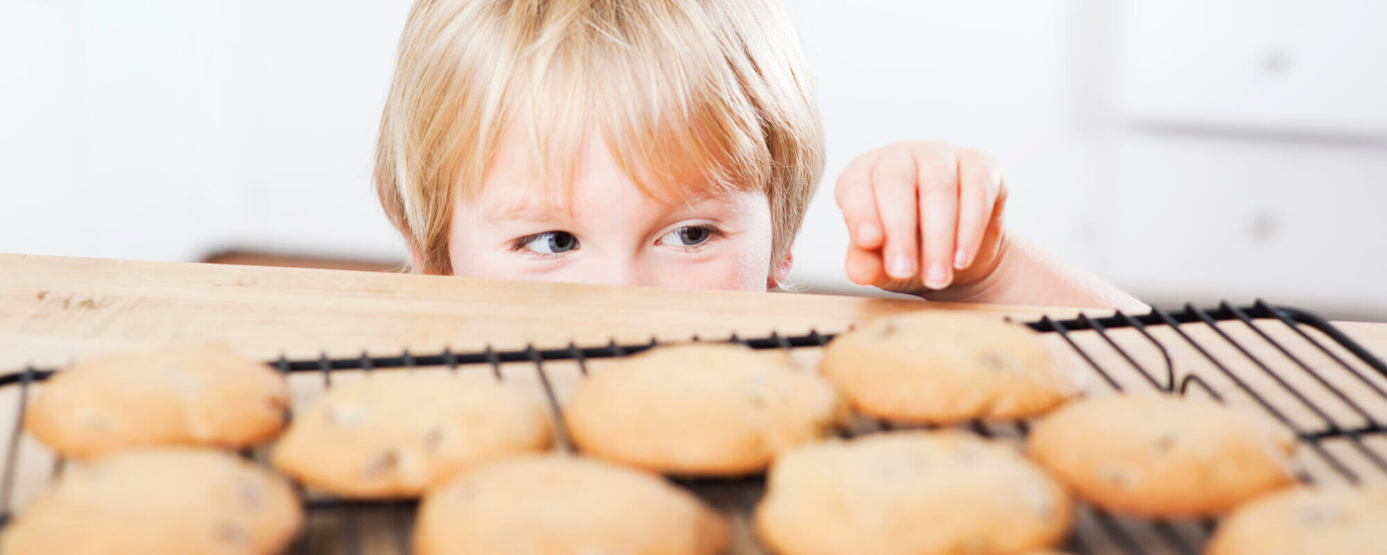 Little boy peeking over counter and sneaking a cookie.