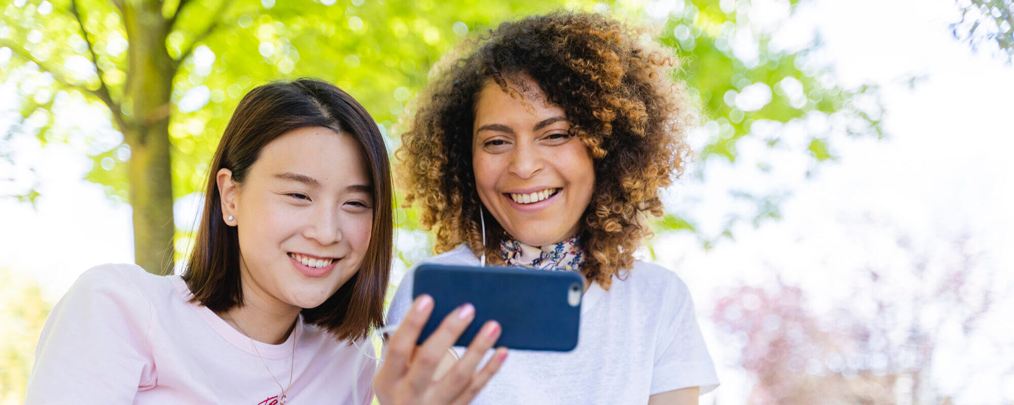 Two happy women with cell phone and earphones in park