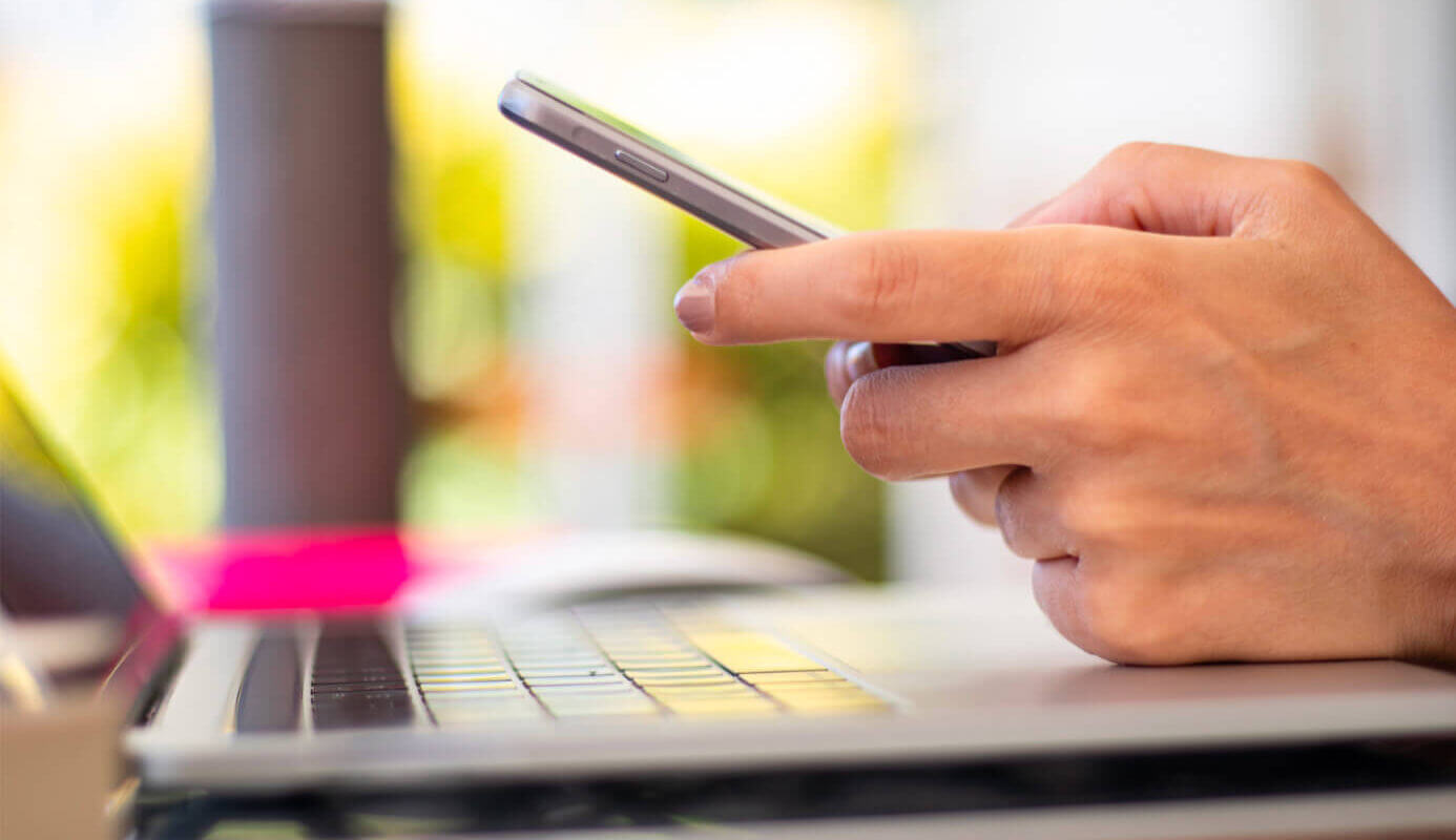 Hand using a mobile phone, leaning on a laptop keyboard.