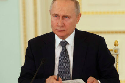 Russian president Vladimir Putin holds a pen and a notes card.